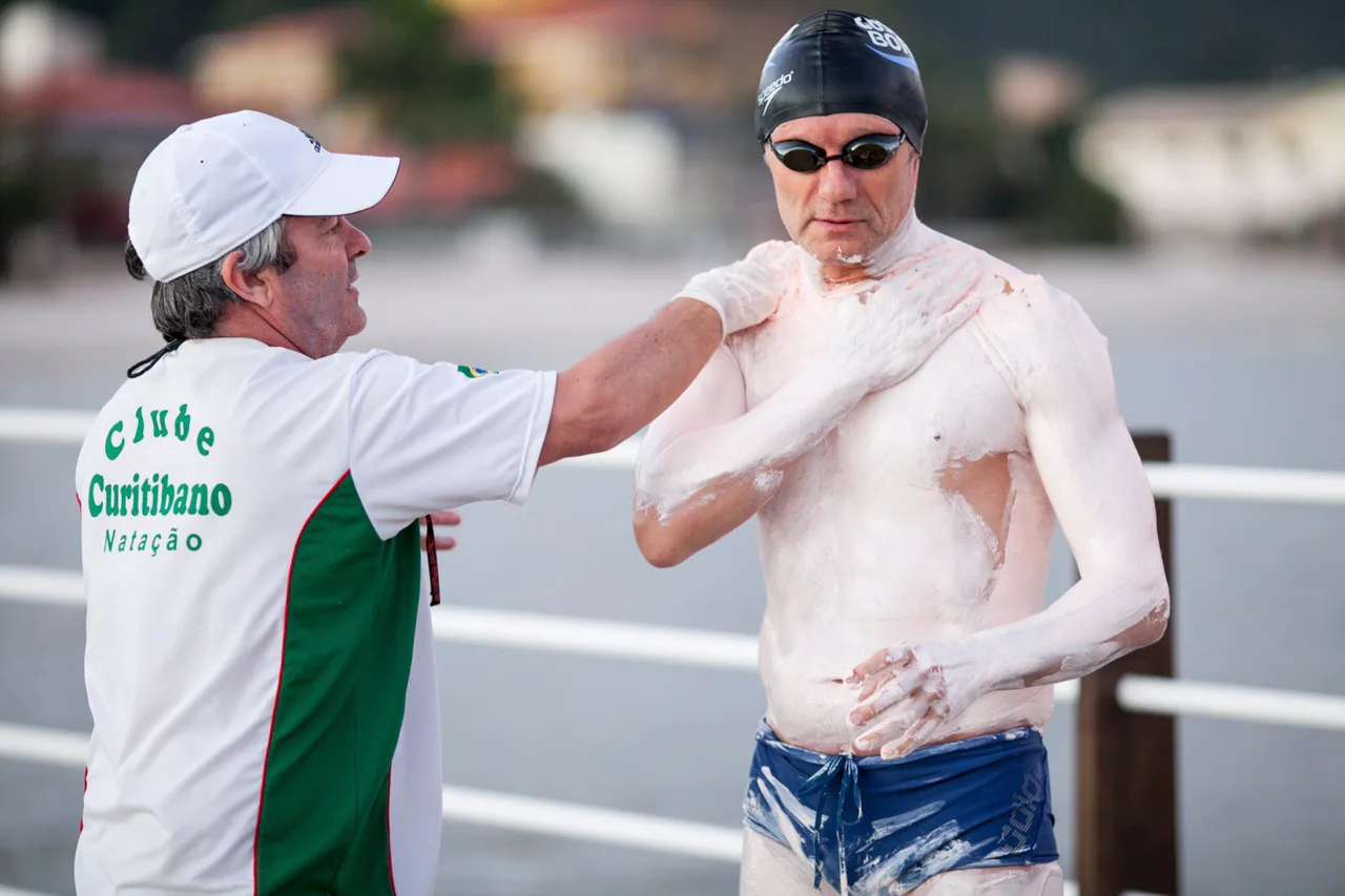 Antes da viagem para a Inglaterra, Joel intensificou os treinamentos no mar. Aqui, um registro da preparação no litoral de Santa Cantarina. O amigo de Joel e companheiro de viagem, Antonio Carlos, ajuda o nadador a passar uma pasta que protege o corpo das baixas temperaturas da água, necessária para a travessia do Canal da Mancha.
