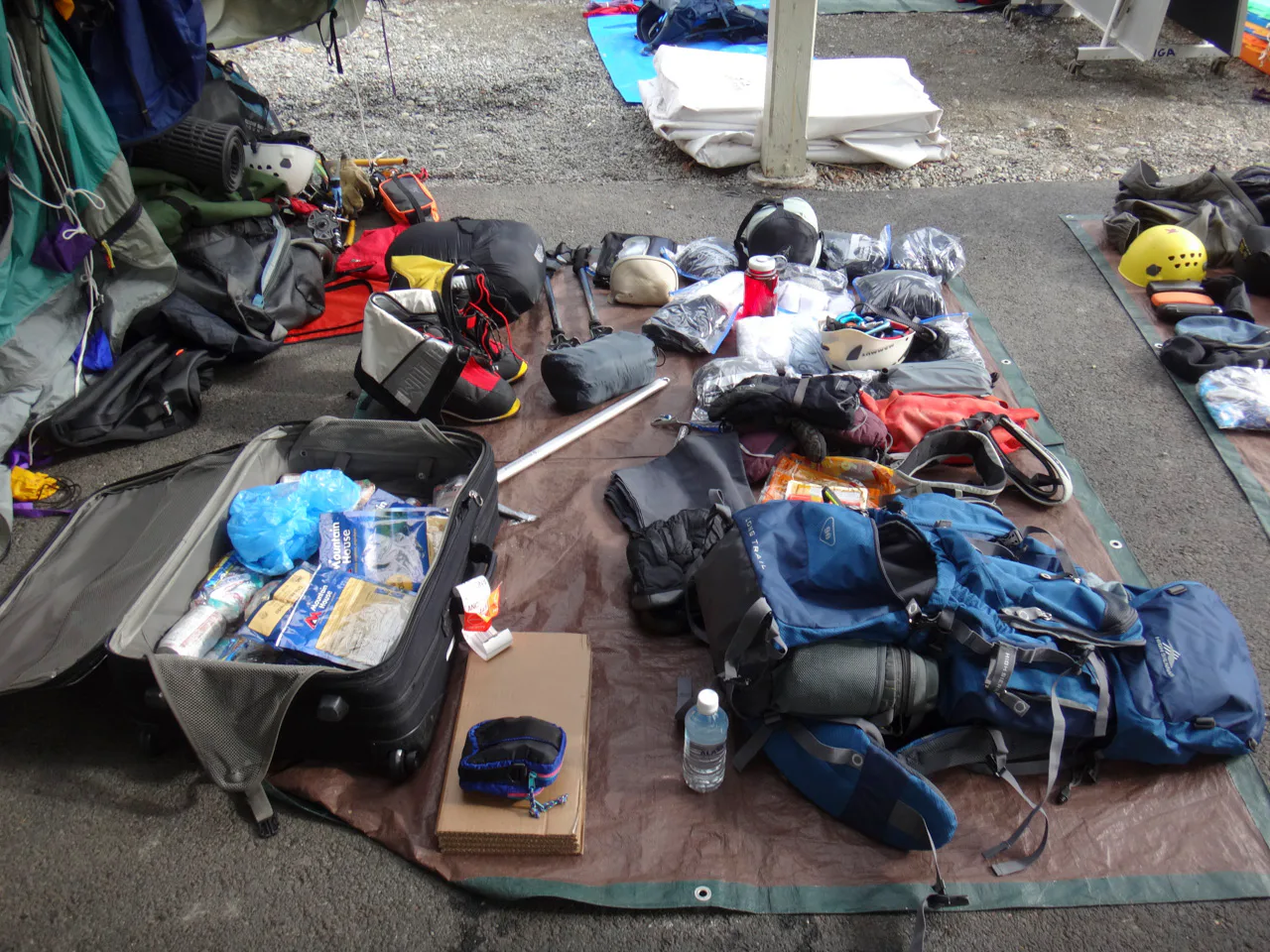 A bagagem de Joel sendo inspecionada antes da saída de Talkeetna. Para o trekking, o montanhista precisa considerar a comida para os 21 dias de excursão e o peso que precisará carregar na subida. Além da mochila, a bagagem é carregada em trenós ligados ao corpo dos trekker por cordas. Itens acessórios como barracas, utensílios de cozinha e outros são divididos entre os membros do grupo para distribuir melhor o peso de cada bagagem.